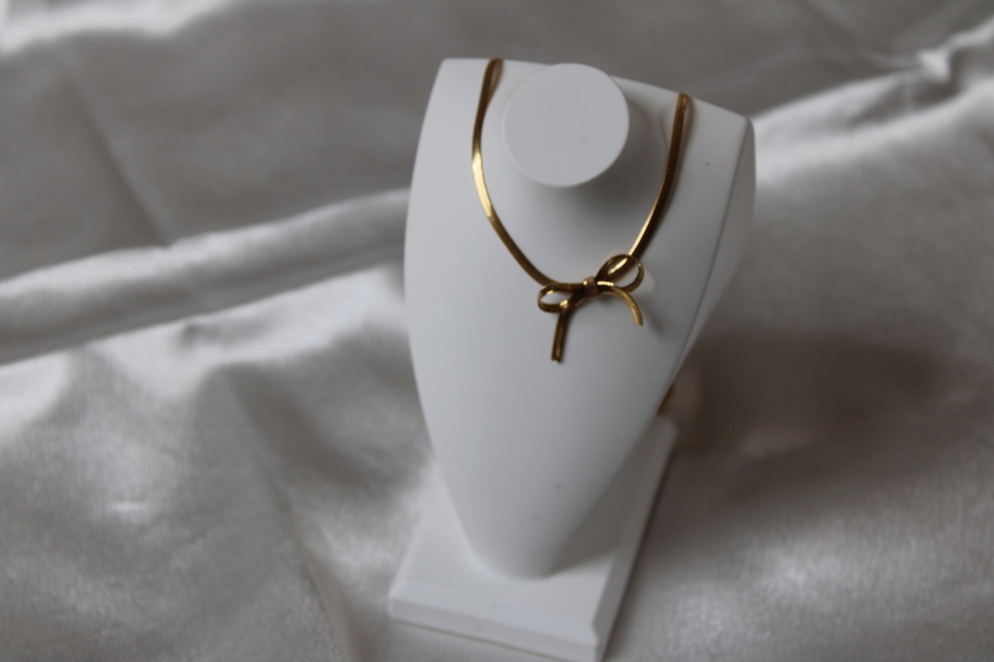 Goldfarbene Kette mit Schleife  auf weißem Satin.